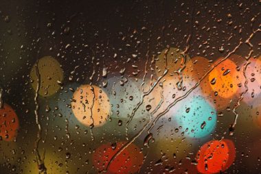 Close-up of raindrops on glass with blurred colorful city lights in the background.